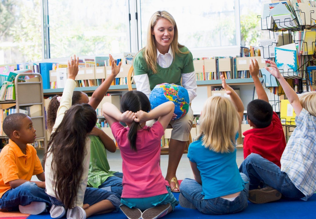 Kindergarten teacher and children with hands raised in library